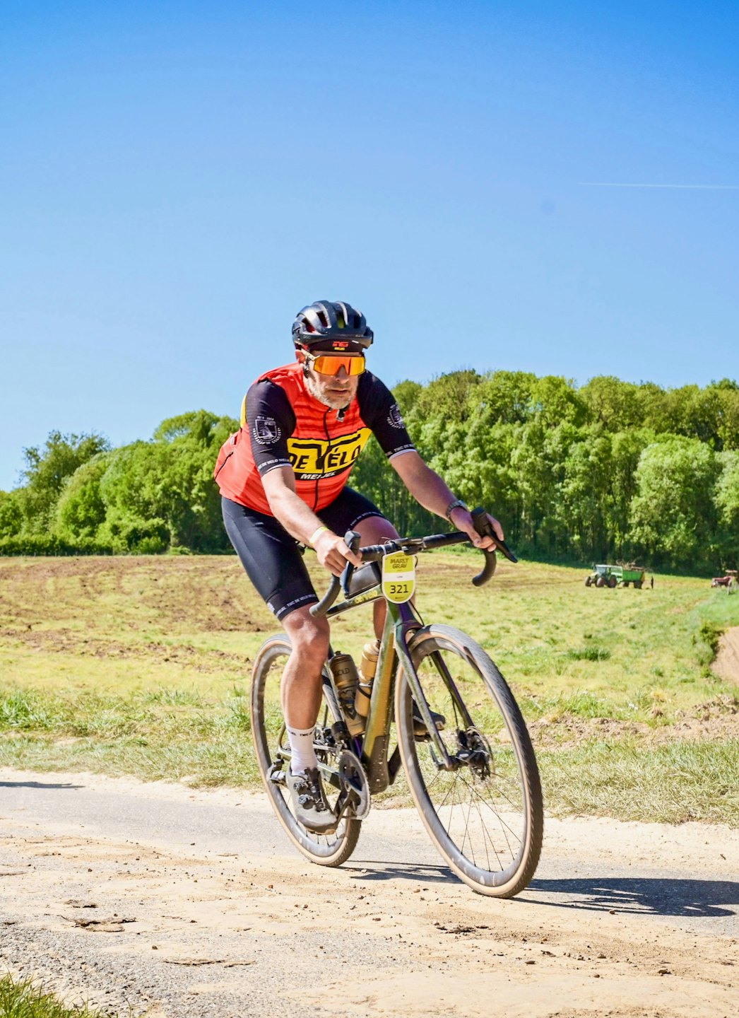 Radsportler im orangenen Trikot fährt Gravelbike auf Schotter.