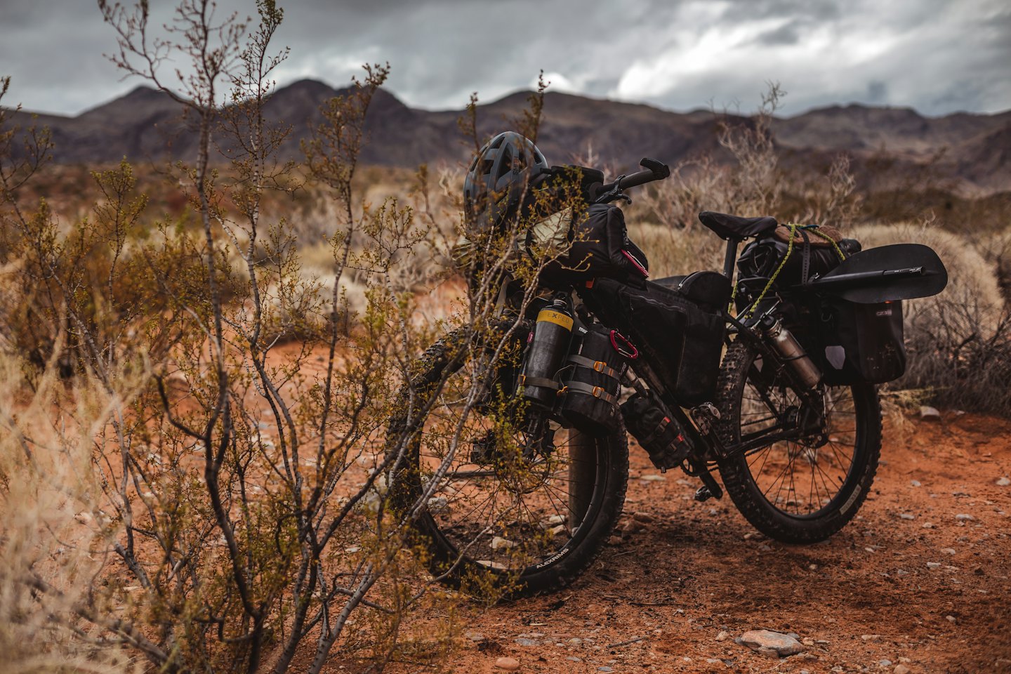 Ein beladenes Bikepacking-Fahrrad mit Ausrüstung steht auf Wüstenboden.